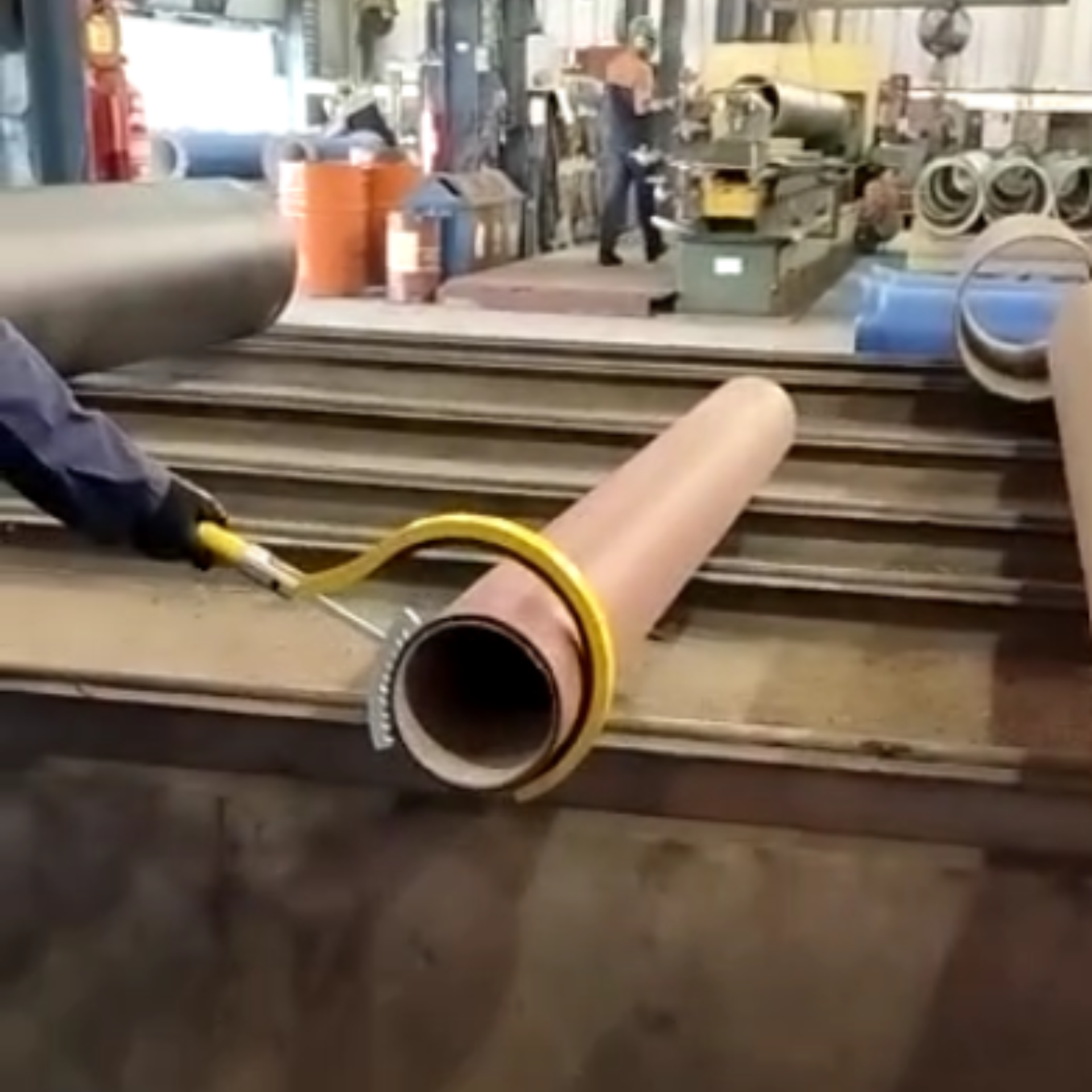 Operador utilizando o Bastão Garra Pega Tubo para orientar tubulações com segurança, mantendo distância segura e controle preciso da carga cilíndrica.