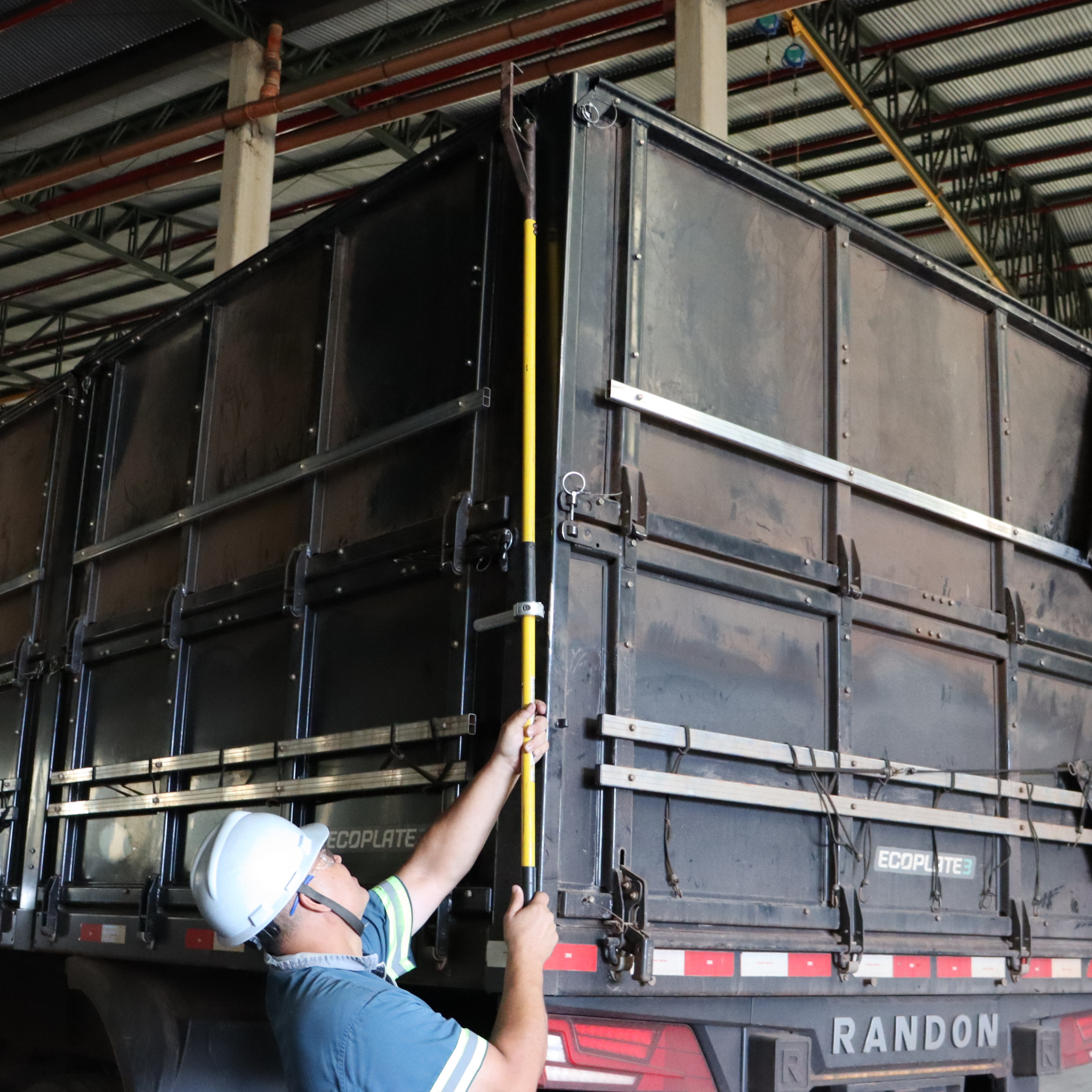 Operador utilizando o Bastão Graneleiro AGMOV para manobrar tampas laterais de caminhões graneleiros com segurança e precisão.